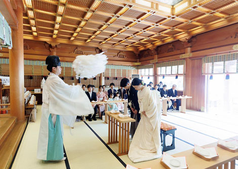 神社での神前結婚式にて、神職が大麻（おおぬさ）を振って新郎新婦を祓い清めている様子