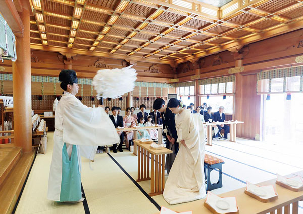 神社の本殿で行われる神前式にて、神職から修祓（お祓い）を受ける新郎新婦。