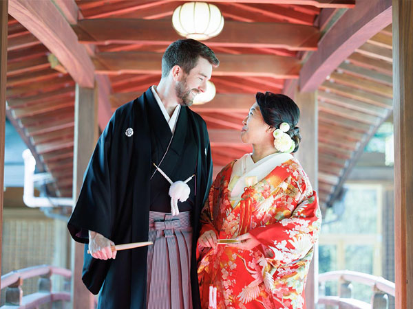 湯島天神の朱塗りの渡り廊下で向かい合う色打掛の新婦と紋付袴の新郎