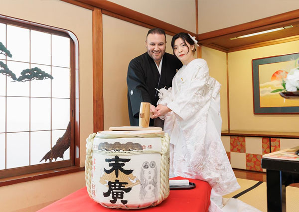 料亭の和室で末廣の菰樽を前に鏡開きをする新郎新婦