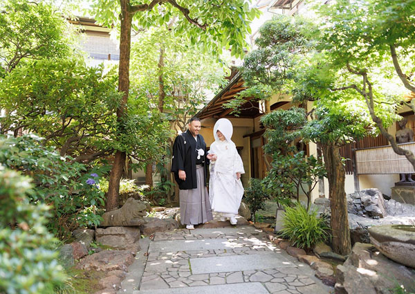 茶寮一松の緑豊かな庭の石畳を歩く白無垢姿の新婦と新郎