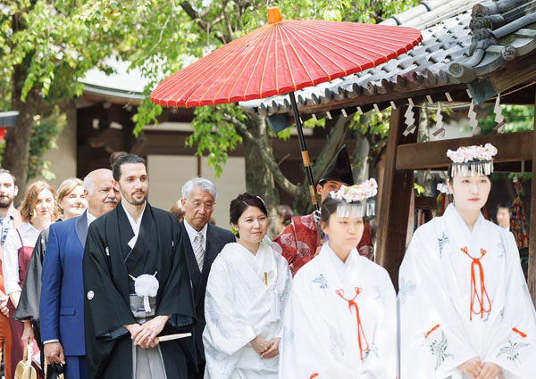 牛嶋神社で赤い番傘のもと参進する白無垢の新婦と外国人参列者