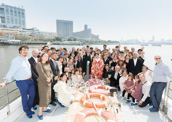 屋形船の甲板で手を振る新郎新婦と大勢の家族・ゲストの集合写真