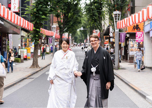 神楽坂の商店街を手をつないで歩く白無垢の新婦と紋付袴の新郎