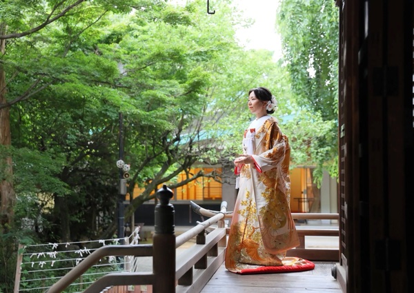 青もみじに囲まれた神社の回廊に立つ、金糸の鳳凰柄の打掛を着た花嫁