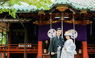 神社の前に立つ紋付袴を着た新郎と白無垢の花嫁